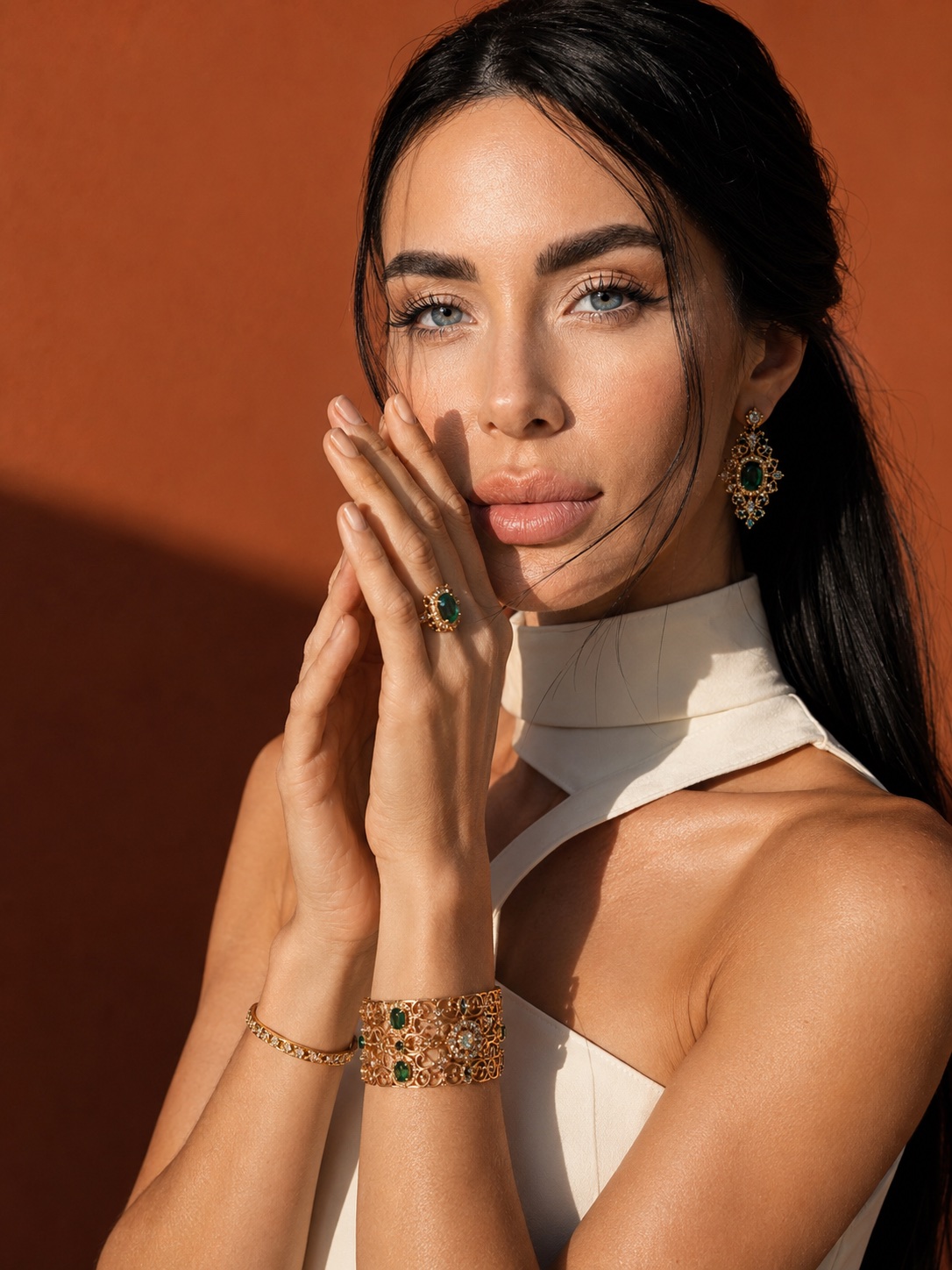 Emerald and gold jewelry editorial against a terracotta wall