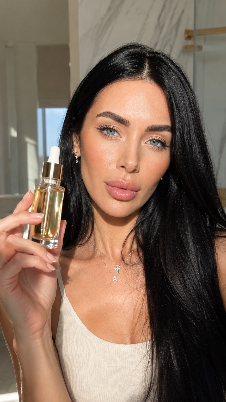 Facial oil held to camera in a bright marble bathroom
