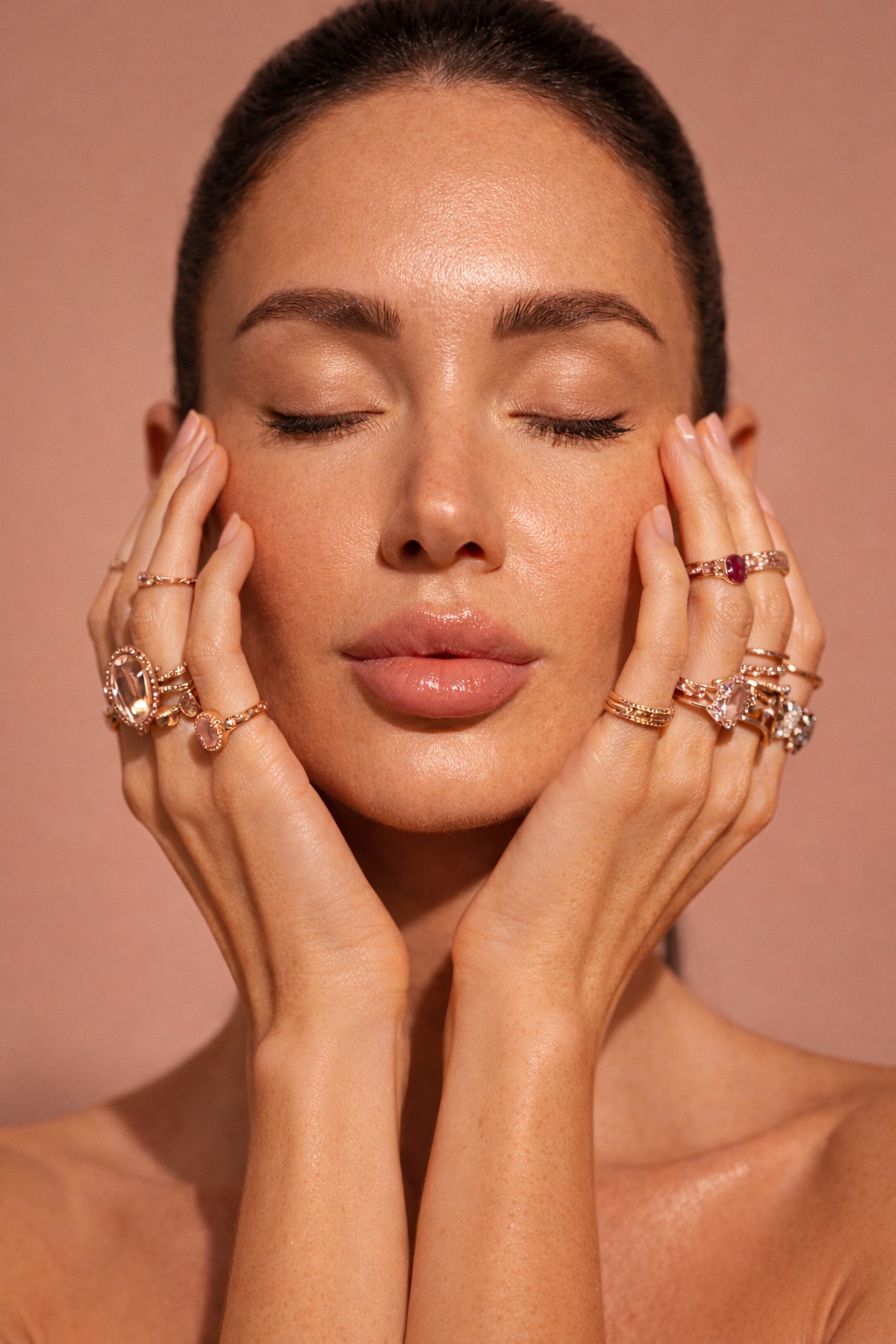 Stacked gold rings framing the face on a blush ground